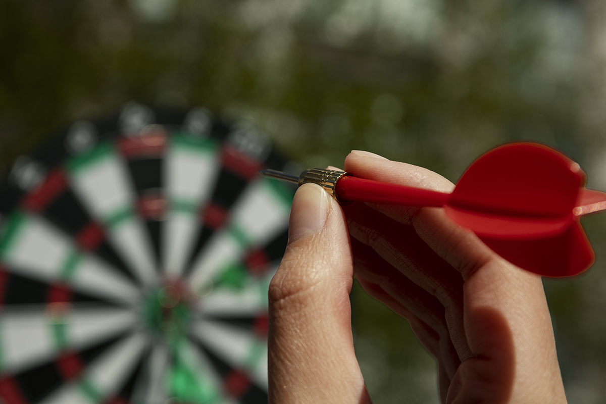 Closeup of a hand aiming an arrow at a dart board.